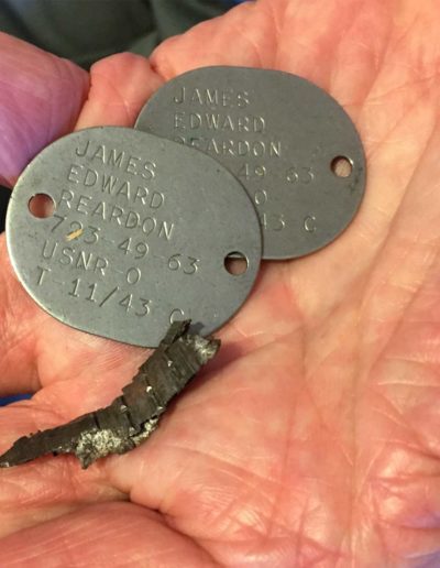 James Reardon holds his dog tags from WWII with a piece of shrapnel he found on the deck of his ship.